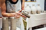 A potter handling a wet clay pot, smoothing the bottom and preparing it for kiln firing.