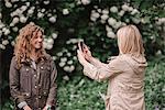 A woman taking a photograph using a smart phone of her companion on a country path.