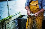 A fisherman in yellow waders extracting a fresh caught fish from the net.