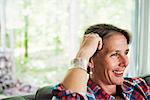 A woman in a check shirt sitting on a sofa reading a book.