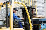 Forklift driver loading pallet onto truck at packaging factory