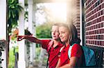 Twin brother and sister sitting on bench pointing, on first day of new school year