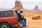 Young man sitting on four wheel drive boot playing acoustic guitar, Monument Valley, Arizona, USA