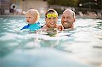 Portrait of a smiling mid-adult man swimming with his two young sons in a back yard swimming pool.