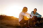 Two young women take a break from their sunrise jog along the cliffs to sit and have a cheerful discussion.