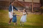 Two little girls have fun playing ring-around-the-rosie with their smiling mother on a grassy lawn.