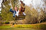 Happy young woman swinging on a wooden rope swing.