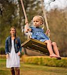 Mother pushing her daughter on a wooden swing.