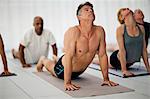 Group of yoga class attendees stretch upward halfway through a salute to the sun routine.