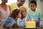 Senior man blowing out his birthday candles with his family.