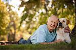 Happy elderly man lying down with his dog in a sunny garden.