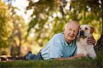 Happy elderly man lying down with his dog in a sunny garden.