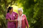 Happy young nurse helpfully assisting an elderly patient to walk outside.