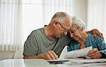 Anxious elderly couple try to comfort each other as they are worried about a bill that they have received.