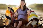 Smiling young woman sitting with her two daughters on a beach.