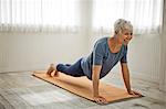Mature woman grins as she does a few push-ups on her yoga mat.
