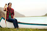 Happy woman sitting on a canoe next to a lake.