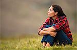 Portrait of a thoughtful mid adult woman sitting in a grassy field.