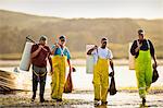 Group of fisherman on the beach with bags of shellfish.