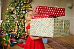 Young girl carrying a stack of Christmas presents.