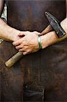 Man in a leather apron holding a hammer.