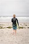 Rear view of a boy carrying a bodyboard, walking into the ocean.
