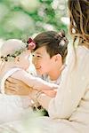 A woman, a boy and baby girl with a flower wreath on her head, sitting in a garden.