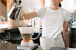 Woman wearing a white apron standing in a coffee shop, making filter coffee.