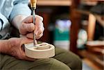 A violin maker using hand tools to smooth and finish a new wooden violin headstock, curled scroll of wood.