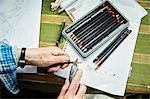 A person using a sharp blade, a craft knife, to sharpen lead pencils. Sketches on paper.