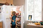 Family preparing breakfast in a kitchen, boy standing at an open fridge.