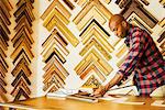 Man working at a picture framers, a large selection of frames on the walls.