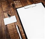 Close-up of blank letterhead in clipboard, badge and pen on wooden table background. Blank template for your design. Responsive design mock-up.