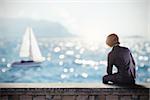 Man sitting on a wall watches the sea with a sailboat