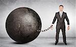 Businessman chained to large ball on grey background