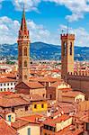 Tower of Palazzo Vecchio in Florence top view to tile roofs of old town. Blue mountains landscape on background. Italy.