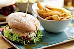 Delicious Burger with Chicken, Lettuce, Grilled Tomato and Cheese Sauce and Bowl with French Fries closeup Outdoors. Focus on Foreground