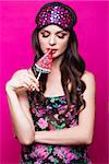 Funny young woman in sleeping mask and pajamas, sweets in the hands on a pink background. The beauty of the face. Photos shot in studio