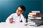 Pensive cute boy with glasses sitting at a table, blue background