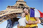 Portrait of smiling mother and child tourists showing flag in the front of Eiffel tower in Paris, France