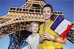 Portrait of happy mother and daughter tourists showing flag against Eiffel tower in Paris, France