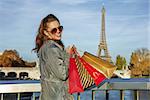 Portrait of happy young elegant woman in trench coat with shopping bags near Eiffel tower