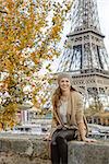 Autumn getaways in Paris. Portrait of smiling young elegant woman on embankment near Eiffel tower in Paris, France sitting on parapet