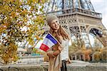 Autumn getaways in Paris. Portrait of smiling young elegant woman on embankment near Eiffel tower in Paris, France showing flag