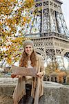 Autumn getaways in Paris. Portrait of smiling young tourist woman on embankment near Eiffel tower in Paris, France with map
