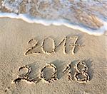 2017 2018 inscription written in the wet beach sand with sea water wave. Inscription 2017 and 2018 on a beach sand, the wave is almost covering the digits 2017.