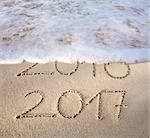 2016 2017 inscription written in the wet beach sand with sea water wave. Inscription 2016 and 2017 on a beach sand, the wave is almost covering the digits 2016.