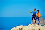 couple of travelers with backpack standing on the cliff against sea and blue sky at early morning