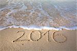 Inscription 2016 on a beach sand, the wave is almost covering the digits 2016.