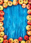 Frame of fresh red apples on  painted blue wooden background with copy space for text in center, top view